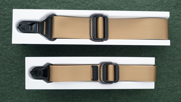 Two tan webbing straps with black plastic side-release buckles displayed on white cards against a green background.