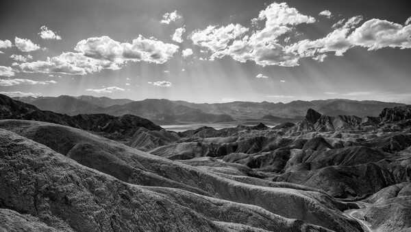 Dramatic black and white landscape of deeply eroded badlands with layered terrain under a cloudy sky.