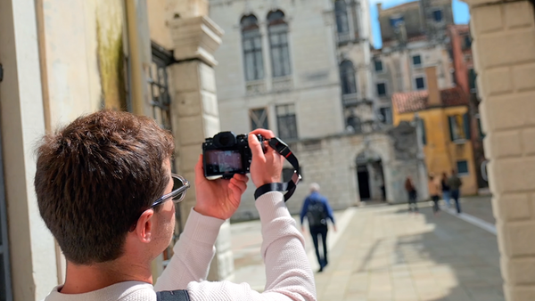Photographer holding a camera at arm's length to frame a historic European plaza with classical architecture.