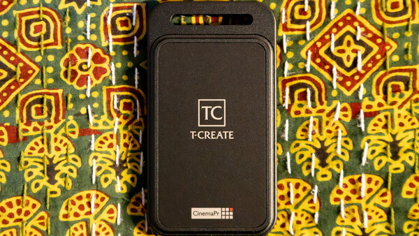 T-CREATE portable device with black casing displayed on colorful patterned fabric background.
