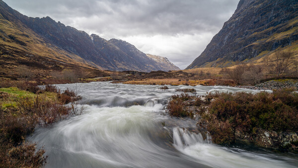 Mountain river flowing through a valley with dramatic peaks and overcast sky.