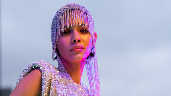 Portrait of a person with beaded braids and bold makeup against a twilight sky with warm and cool color grading.