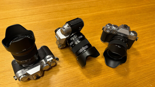 Three vintage rangefinder cameras with attached lenses displayed on a wooden surface.