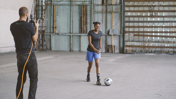 Photographer shooting a soccer player posing with a ball in an industrial space.