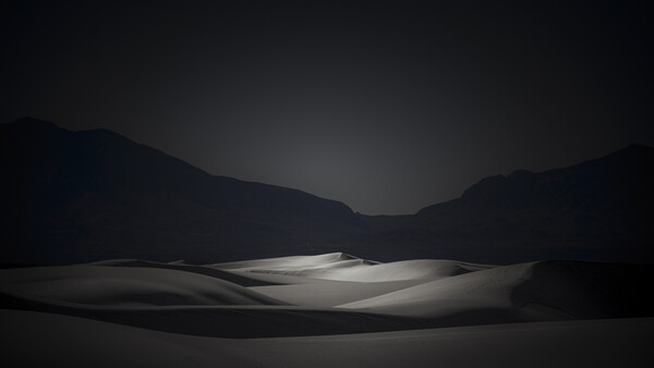 Minimalist landscape with illuminated ground plane and dark mountainous silhouettes against twilight sky.