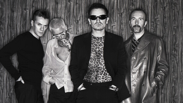 Four men posed against a wooden backdrop in black and white portrait photography.