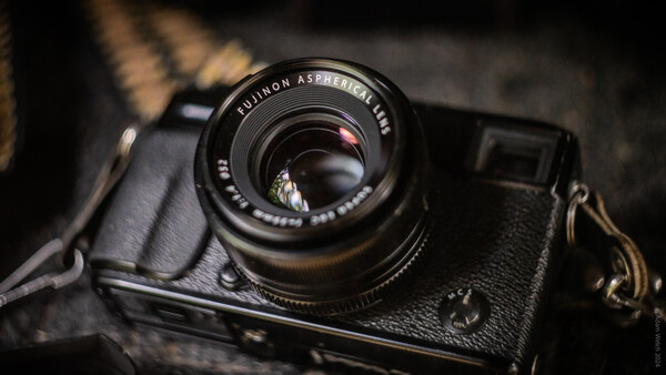 Vintage rangefinder camera with Fujinon lens mounted on dark leather strap against textured background.