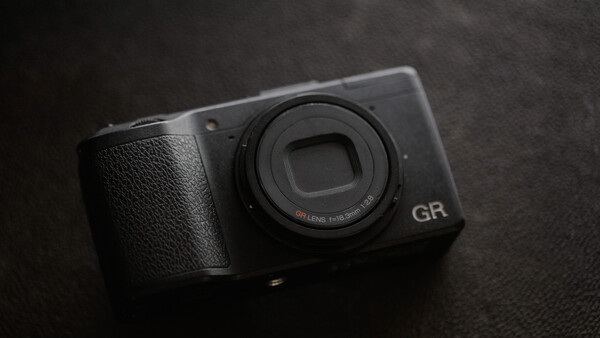 Ricoh GR compact camera with fixed lens on dark textured surface.