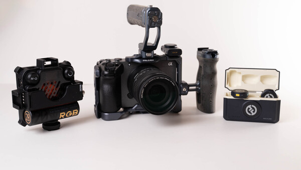 Video production kit with cinema camera, RGB light, wireless microphone, and accessories on white surface.