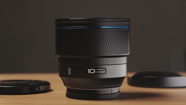 A 10mm prime lens with ribbed rubber grip and metal barrel displayed on wooden surface with soft studio lighting.