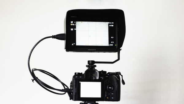 Professional video camera with external monitor mounted on top via cable.