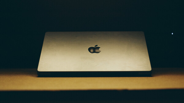 Gold MacBook Pro closed on wooden surface against dark background with dramatic side lighting.