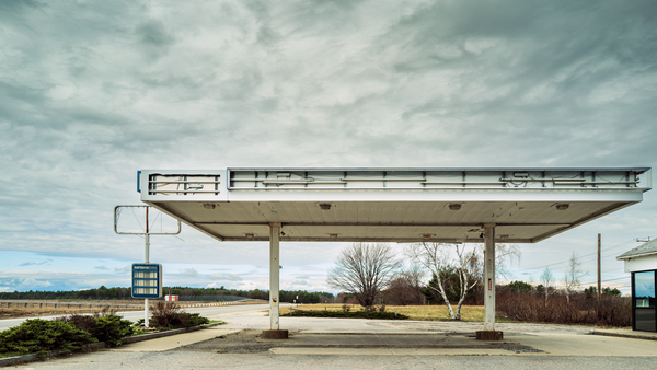 Abandoned gas station canopy with weathered concrete structure under overcast sky.