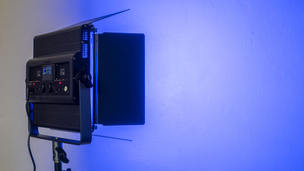 Professional LED panel light mounted on stand with blue gel filter and control panel visible.