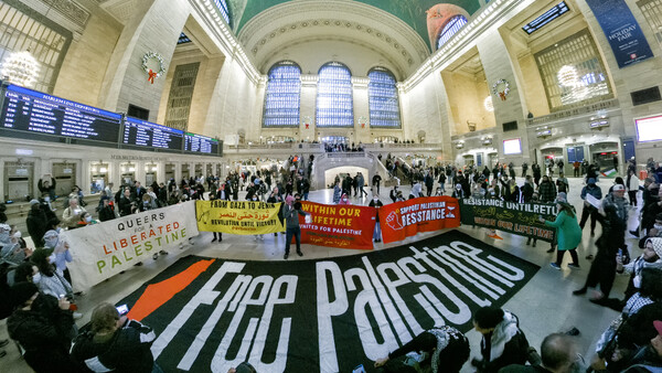 Pro-Palestine demonstration in a grand station with large banners and dozens of participants.