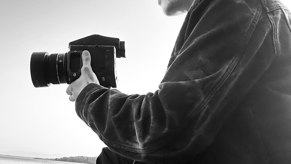 Photographer holding a DSLR camera, shooting from a boat on calm water in black and white.