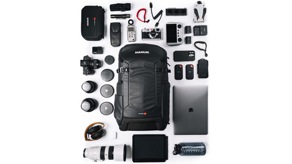 Flat lay of professional photography and videography equipment including camera body, lenses, backpack, laptop, batteries, and audio gear.