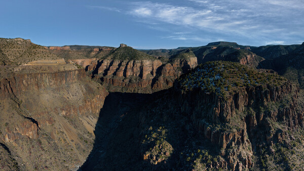 Deep canyon with layered rock formations and sparse vegetation under blue sky.