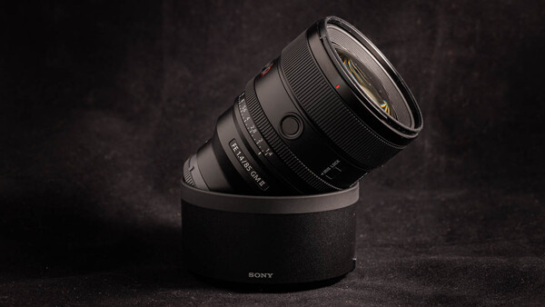 Sony lens mounted on cylindrical black stand against dark textured background.