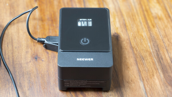 Neewer battery charger with power button and LCD display on wooden surface.