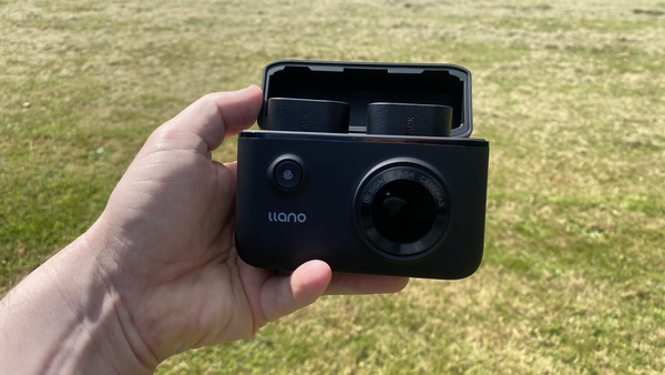 Hand holding an open Ilano compact camera against a grass background.
