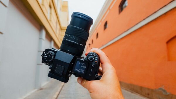 Photographer holding a mirrorless camera with telephoto lens attached, shot from above on an urban street.