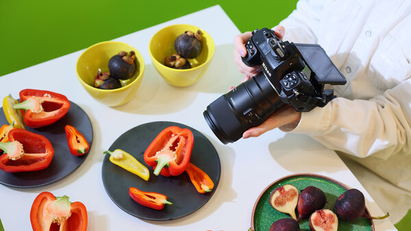 Photographer holding DSLR camera over styled food photography setup with fresh vegetables and fruits.