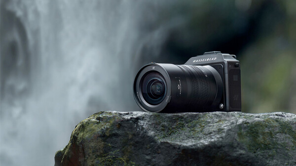 Mirrorless camera with wide-angle lens positioned on a moss-covered rock beside a flowing waterfall.