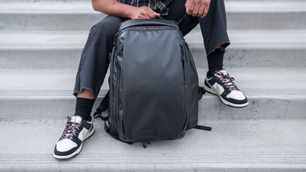 Person sitting on concrete steps holding a dark gray backpack with organizational compartments.