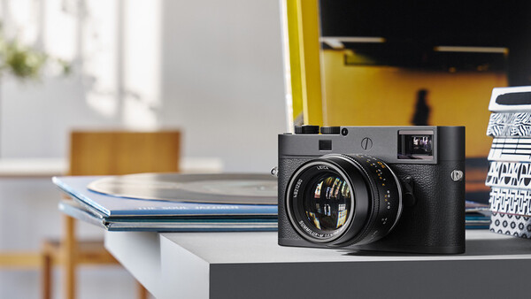 Leica M rangefinder camera with 50mm lens on a white desk with blue notebook and yellow wall backdrop.