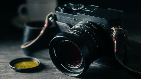 Vintage rangefinder camera with manual lens and yellow filter on dark surface.