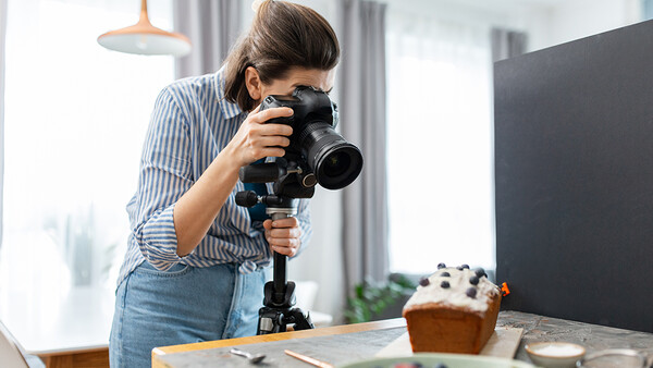 Photographer using a telephoto lens mounted on a tripod while shooting a styled food scene indoors.