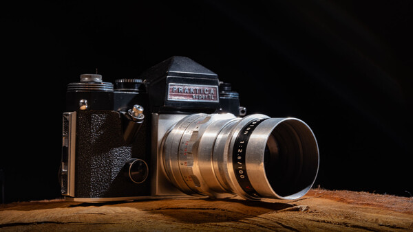 Two vintage rangefinder cameras displayed on a wooden surface against a black background.