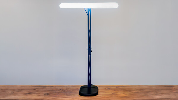 Modern desk lamp with tall dark blue-black stand and white LED panel on wooden surface.