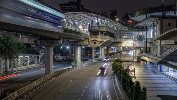 Nighttime urban street scene with elevated highway overpass, wet pavement, and blurred vehicle lights.