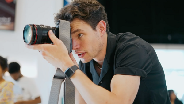Photographer holding a professional camera with telephoto lens up to his eye while composing a shot indoors.