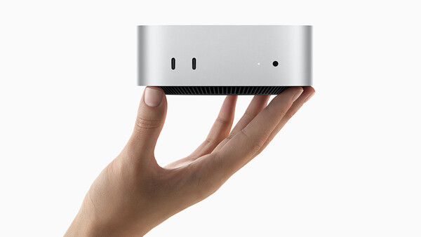 Hand holding a compact silver and black desktop computer against a white background.