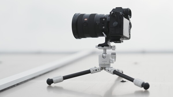 Mirrorless camera with telephoto lens mounted on a compact tripod against a minimalist gray background.