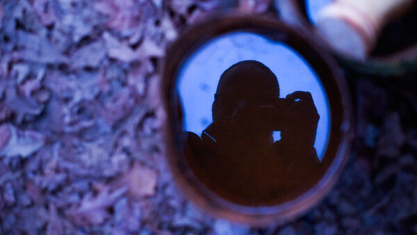 Silhouette of photographer holding camera visible through circular opening in textured wall.