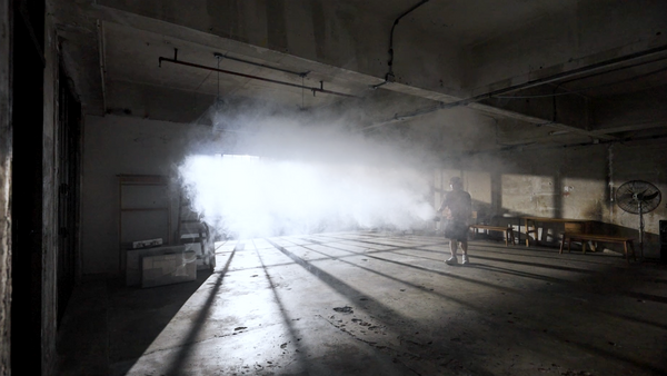 Dramatic light beam streaming through abandoned warehouse interior with concrete floor and industrial ceiling.