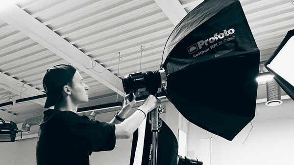 Photographer adjusting a large black Profoto softbox mounted on a light stand in a studio with white ceiling.