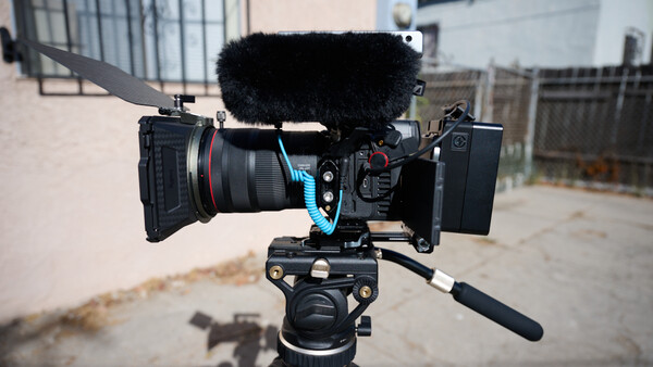 Professional cinema camera rig with follow focus wheel and shotgun microphone mounted on tripod.