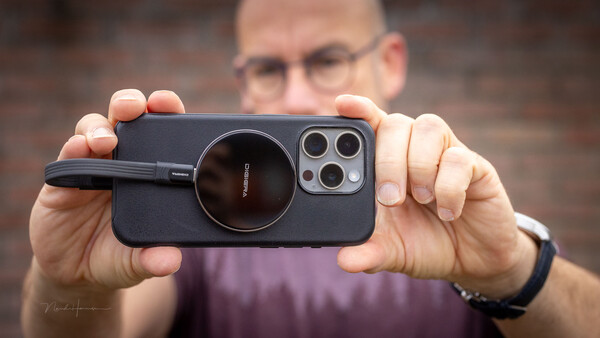 Man holding iPhone with black magnetic lens attachment, displaying triple camera setup.