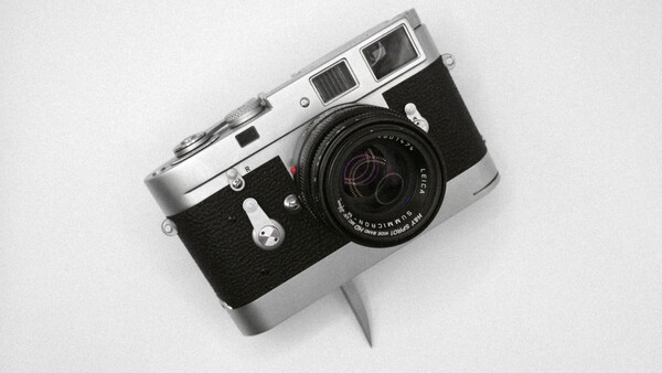 Vintage rangefinder camera with chrome top plate and black body on white background.