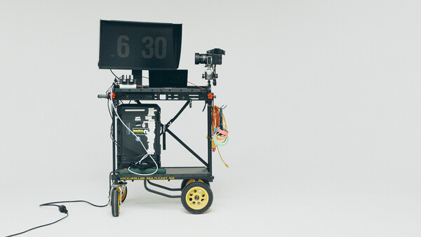 Mobile teleprompter rig on yellow-wheeled cart with monitor displaying timecode display.