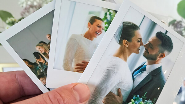 Hand holding instant film photographs of people in various candid moments and poses.