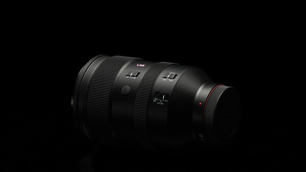 Dark telephoto lens with multiple focus distance markings against black background.