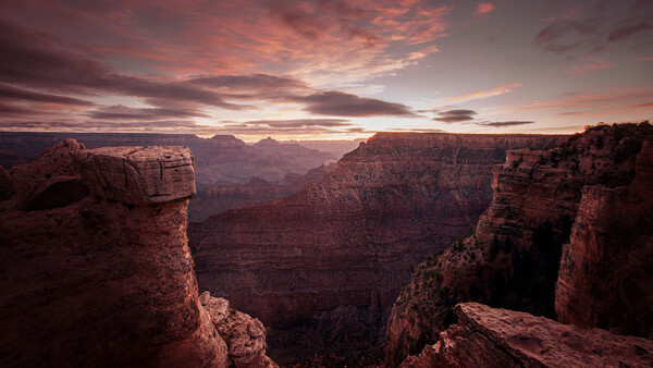 Grand Canyon vista at sunset with layered red rock formations and dramatic pink-orange sky.