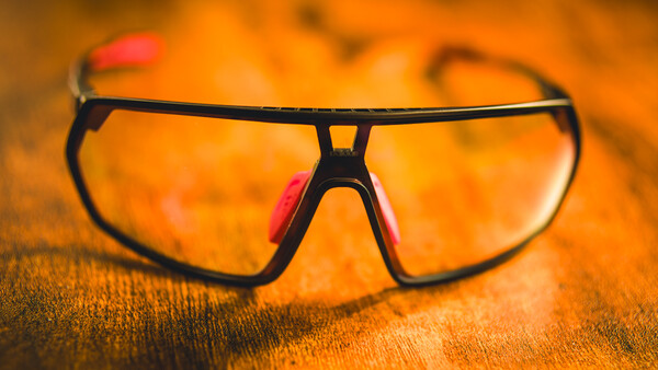 Sunglasses with dark frames and pink accents resting on a textured orange fabric surface.