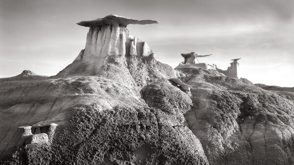 Dramatic black and white landscape of distinctive rock formations with flat-topped peaks rising from eroded badlands terrain.